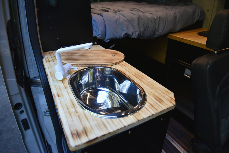 RV rental interior showing a compact kitchen with a wooden countertop, stainless steel sink, modern white faucet, and bed. — photo 2
