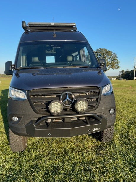 Customized Mercedes Sprinter rv rental van with off-road lights, rugged bumper, and roof rack, parked on grass on a sunny day.