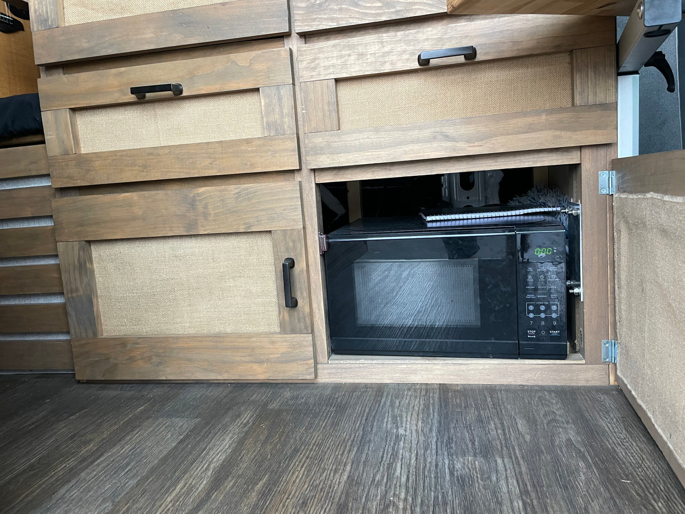 RV rental: Custom wooden cabinetry with burlap inserts and a pull-out microwave, showing efficient camper storage.