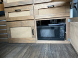 RV rental: Custom wooden cabinetry with burlap inserts and a pull-out microwave, showing efficient camper storage.