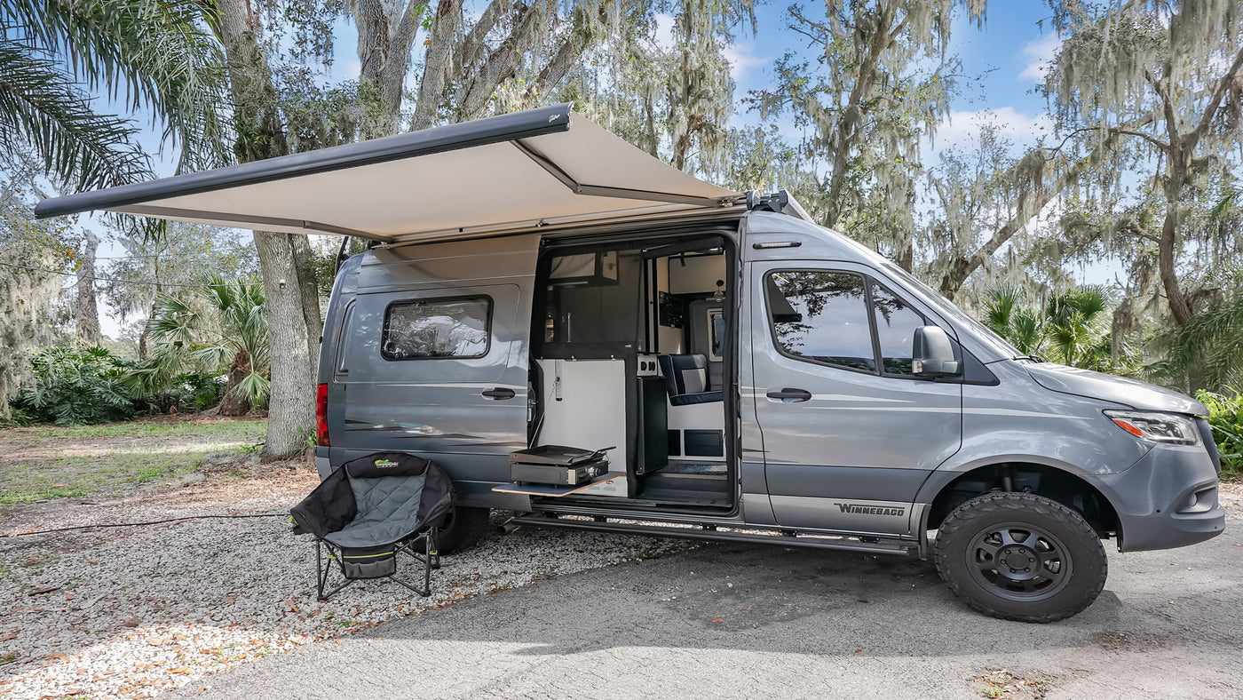 Gray Winnebago camper van with extended awning & outdoor kitchen setup. Great rv rental for camping and travel.