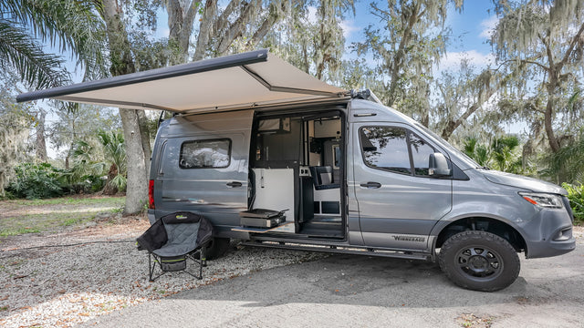 Gray Winnebago camper van with extended awning & outdoor kitchen setup. Great rv rental for camping and travel.
