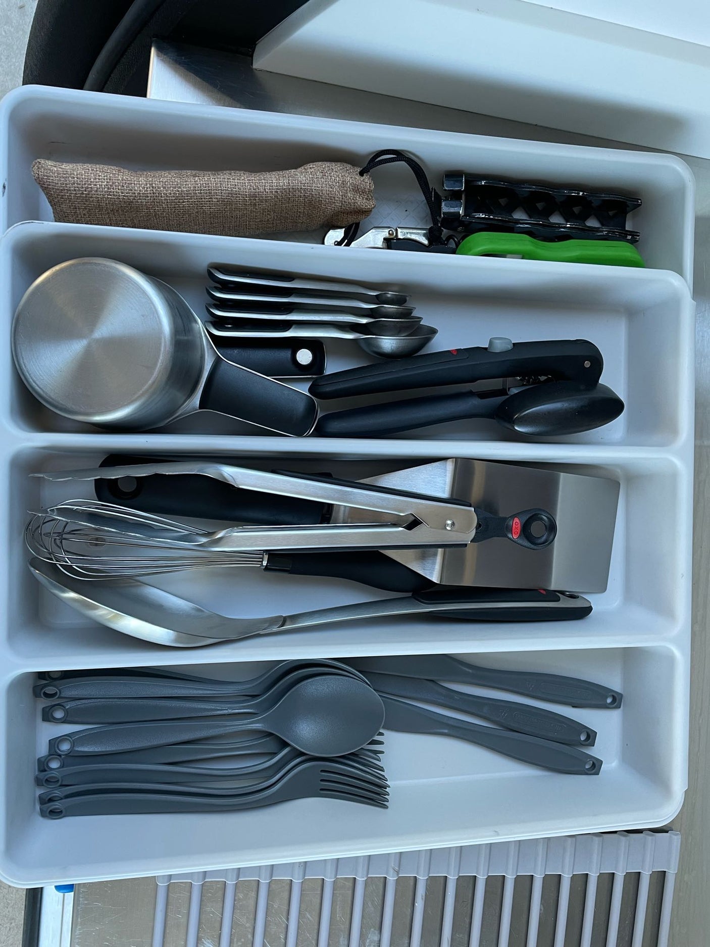 An RV rental's well-stocked kitchen drawer, featuring cookware, tools, measuring implements, and gray plastic cutlery.