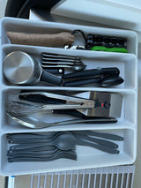 An RV rental's well-stocked kitchen drawer, featuring cookware, tools, measuring implements, and gray plastic cutlery.