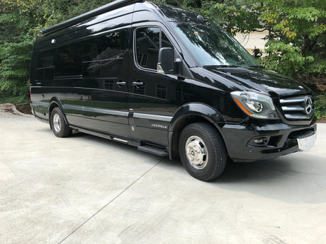 Black Airstream Mercedes Sprinter rv rental van, perfect for travel. Parked on a concrete driveway with trees in the background.