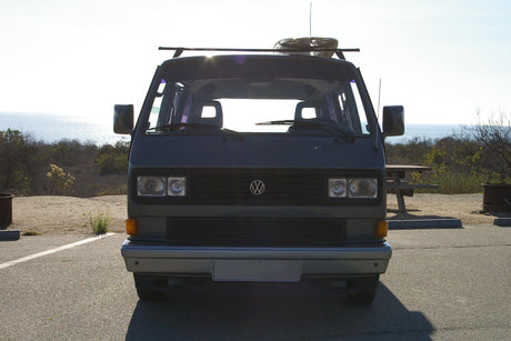 Front view of a gray VW Vanagon camper van parked at a scenic ocean-side campsite. Ideal RV rental for your next adventure.
