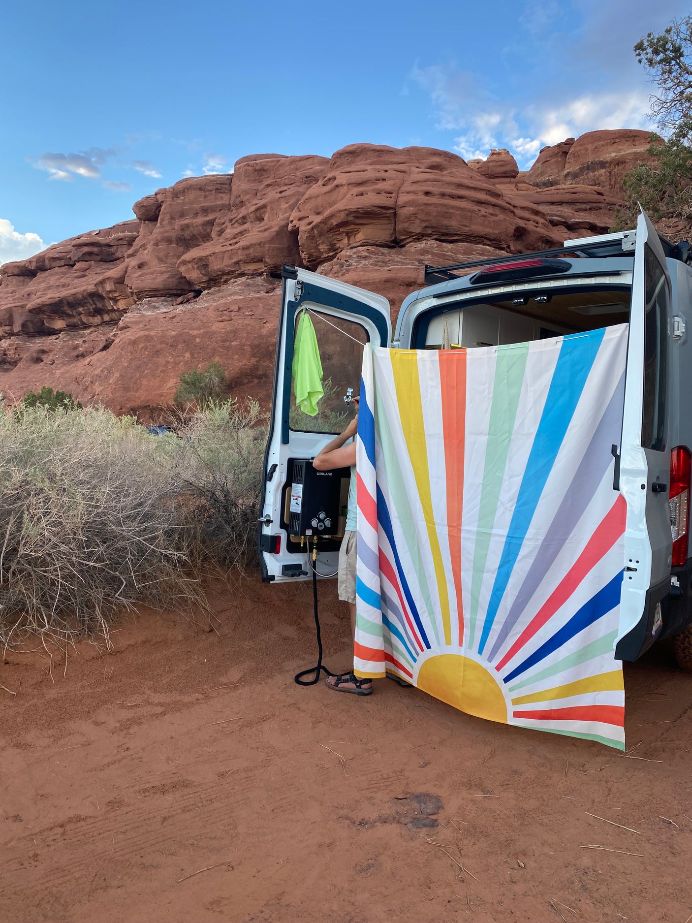 Outdoor shower setup with a portable heater next to an RV rental, set against scenic red rock formations.