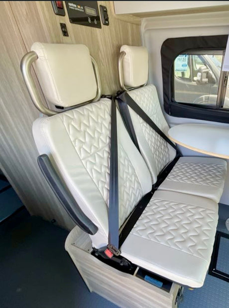 White quilted bench seats with headrests and seatbelts inside an RV rental, featuring a partial dining table.