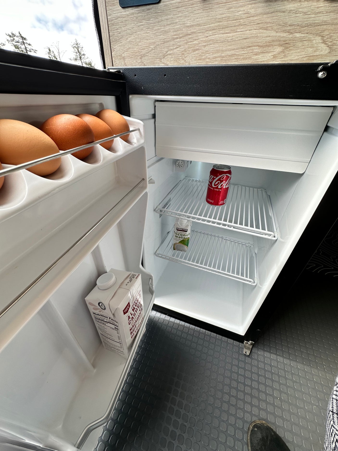 Looking inside a compact rv rental fridge, stocked with eggs, plant-based milk, Coke, and coconut water for the journey.