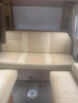 RV rental interior with a light beige dinette, two seats, window with blinds, and wood floor. Comfortable, clean space for your journey.