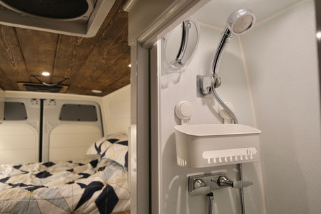 Compact shower with handheld head and mirror, beside a cozy bed with patterned bedding in a modern rv rental.