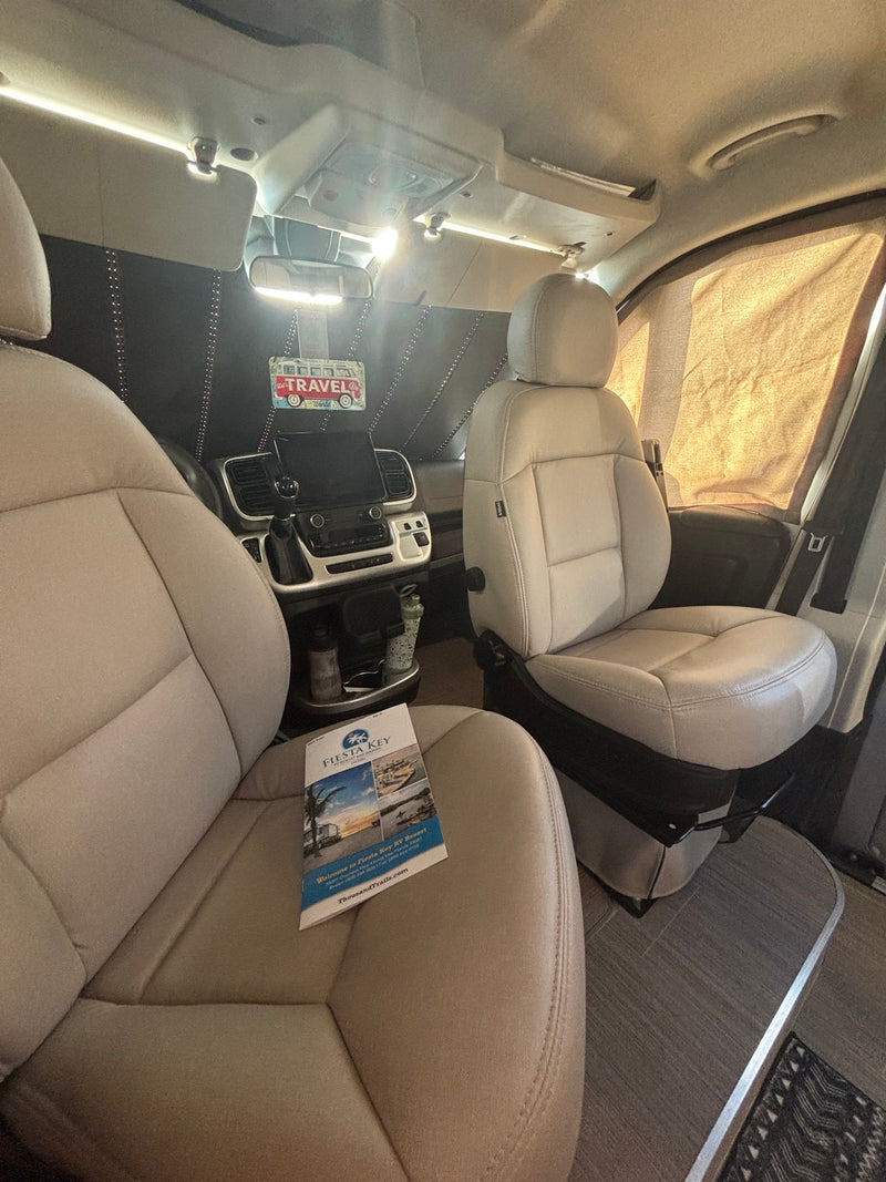 RV rental's front cabin with cream seats, dashboard, 'TRAVEL' sign, and Fiesta Key RV Resort brochure. — photo 9