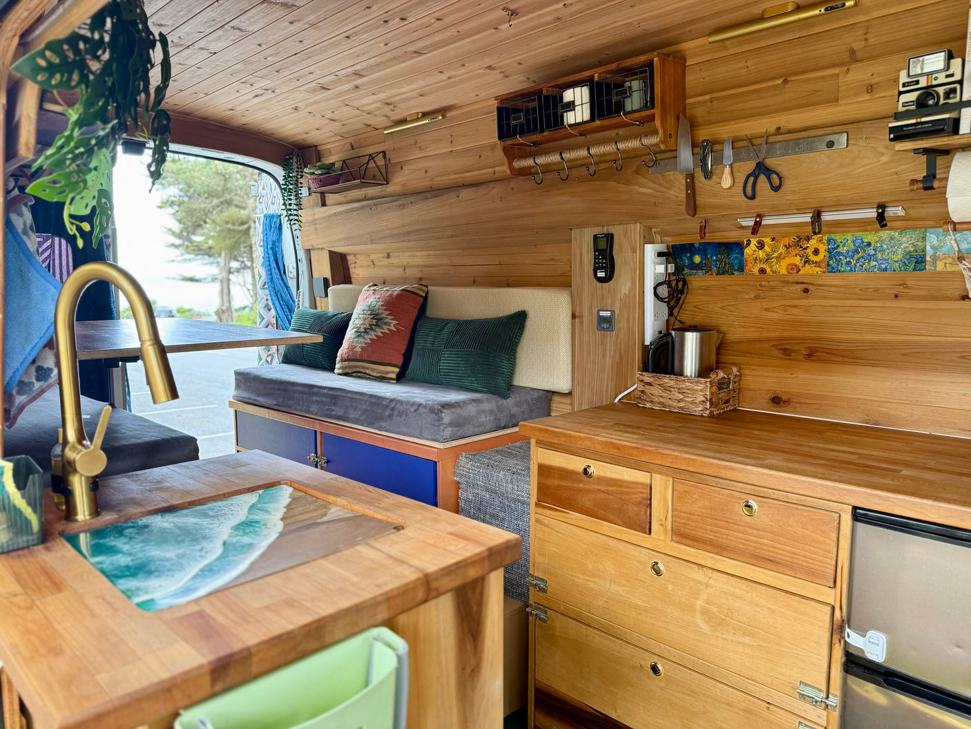 Cozy wood-paneled rv rental interior. Features kitchen with ocean-themed sink, comfortable seating, and custom storage for van life.