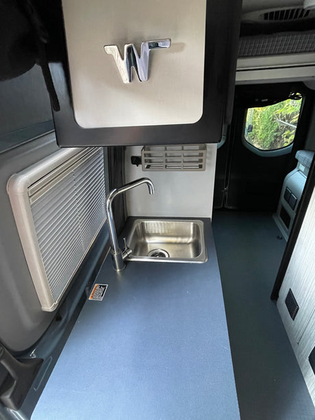 Compact Winnebago RV rental kitchen with stainless steel sink, faucet, and light blue counter.