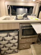 An RV rental kitchen shows a sink, stove, microwave, and uniquely patterned fridge, designed for efficiency.