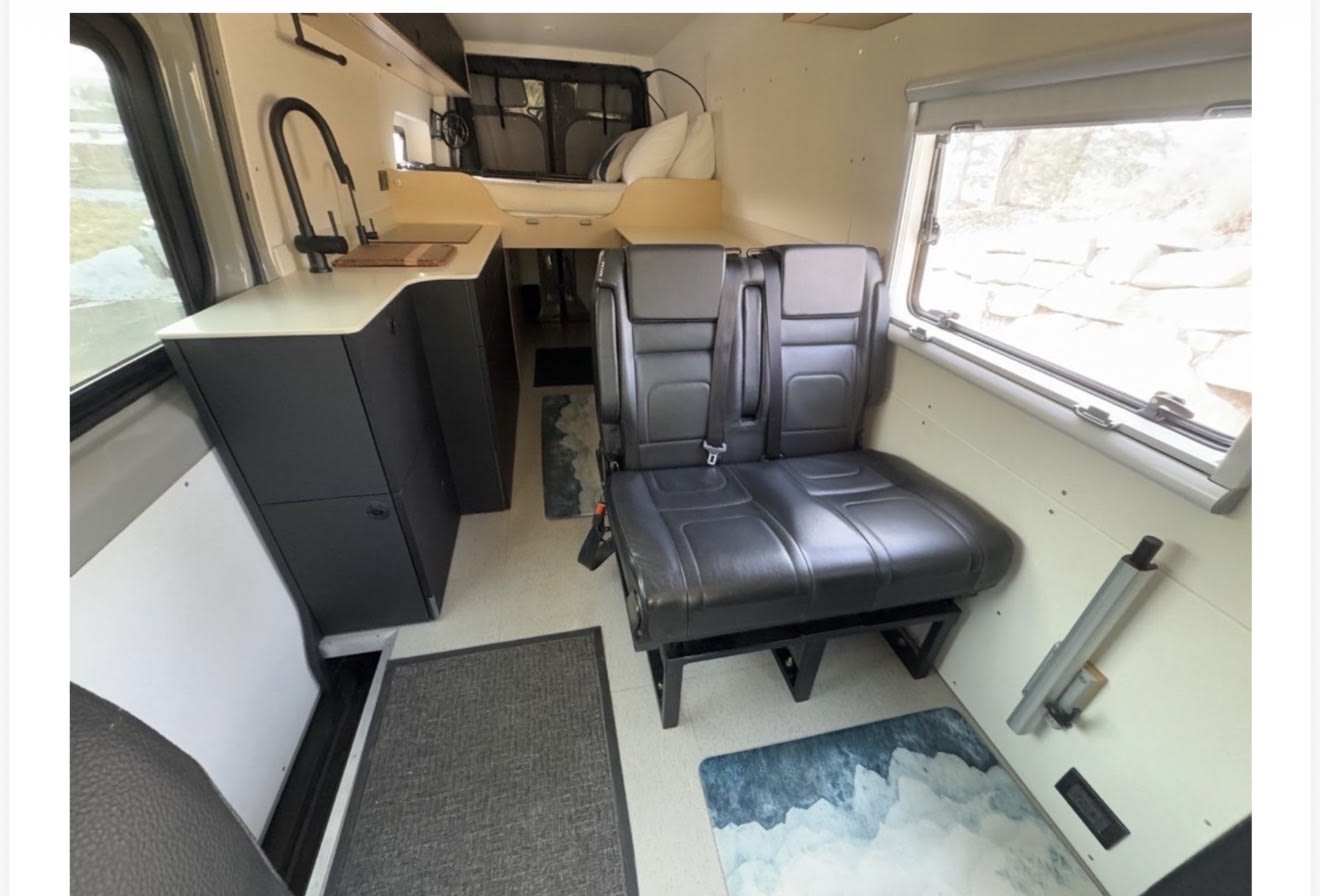 Interior of an RV rental with a kitchenette, passenger seats, and a cozy elevated bed. Perfect for van life adventures.