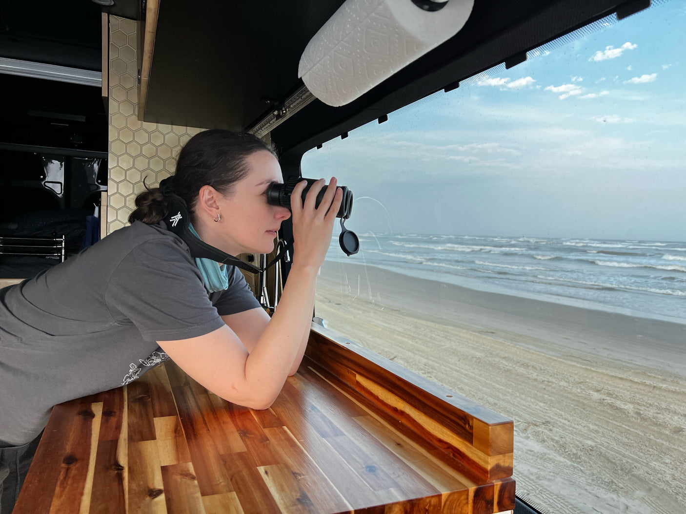 Woman enjoys ocean views with binoculars from her comfortable RV rental by the beach.