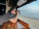 Woman enjoys ocean views with binoculars from her comfortable RV rental by the beach.