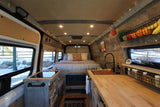 Cozy custom RV rental interior with a spacious bed, fully equipped kitchen, and warm lighting, perfect for van life adventures.