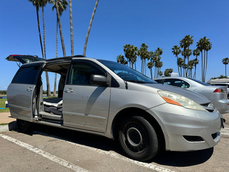 A silver camper minivan with open doors and trunk, revealing its interior bed setup. Ideal rv rental for a sunny adventure.
