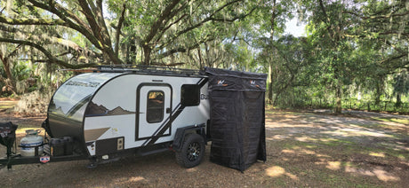 Bushwhacker RV rental camper with a NaturNest privacy tent, nestled in a serene spot among trees with Spanish moss.