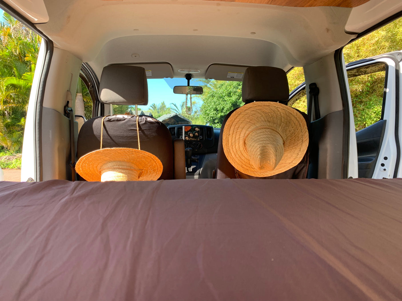 Your next RV rental adventure awaits! Cozy bed, hats on seats, and a tropical view from inside a camper van.