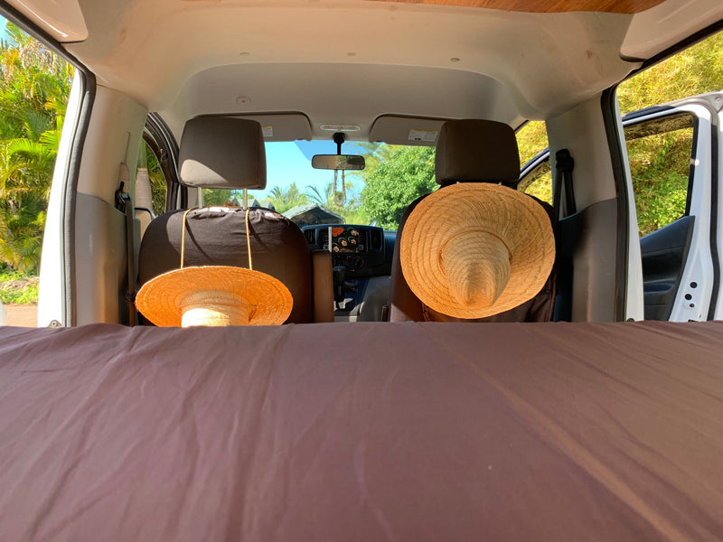 Your next RV rental adventure awaits! Cozy bed, hats on seats, and a tropical view from inside a camper van. — photo 7