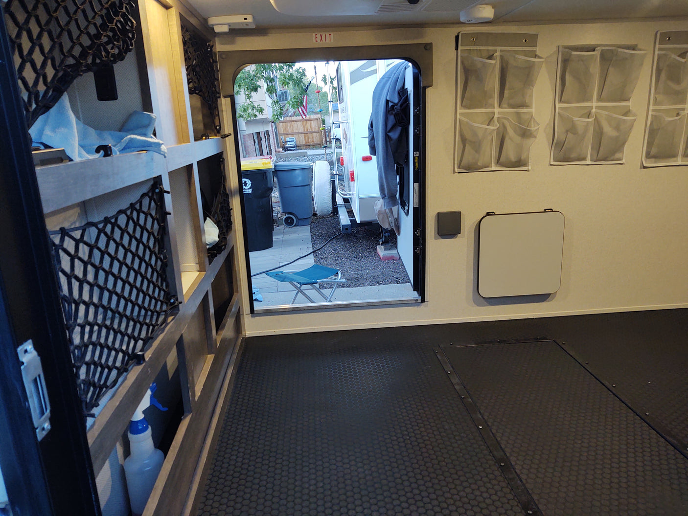 Spacious RV rental interior with organized storage, fold-down table, and black textured floor, looking out rear door.