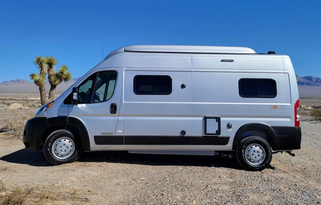 Silver Solis camper van for RV rental, parked in a sunny desert with Joshua trees and distant mountains.