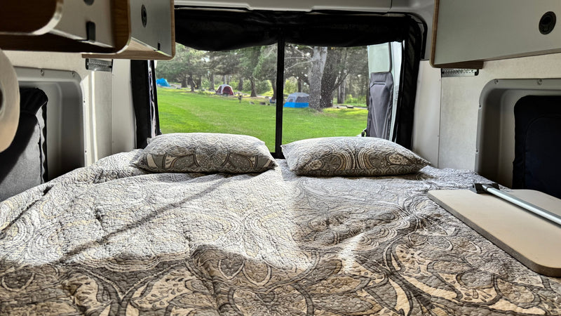  surrounded by other campers.|Explore this RV rental! Open rear van doors reveal a cozy bed — photo 8