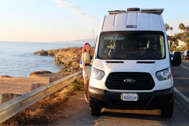 showcasing outdoor shower system with portable water heater and bed.|Relaxing with coffee and a stunning ocean view from an RV rental. Features a full sink and mobile kitchen setup.|Interior of an RV rental kitchen with a large white sink — photo 6