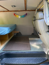 Cozy RV rental interior featuring a bed, vibrant prayer flags, and string lights, with passenger seats visible.