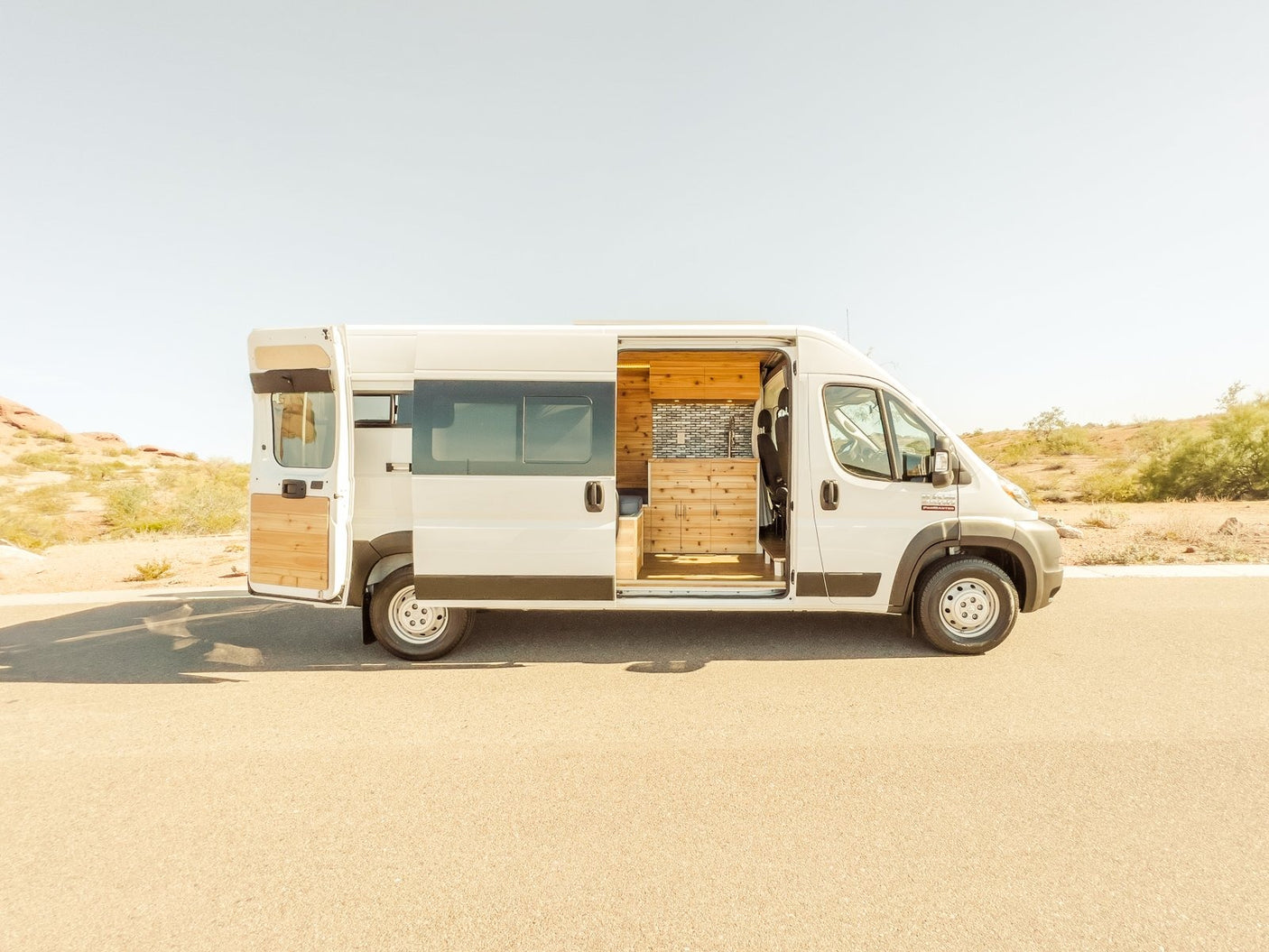White camper van RV rental, side & rear doors open, showcasing a custom wood interior. Ready for your next road trip adventure.