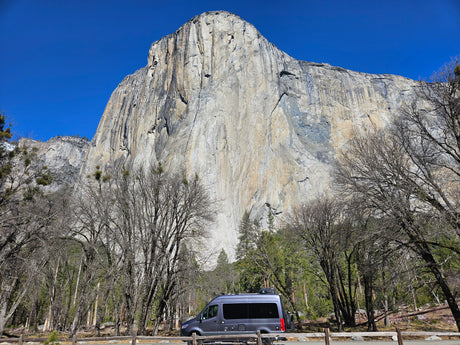 RV rental parked with a view of towering El Capitan in Yosemite National Park, surrounded by bare trees.
