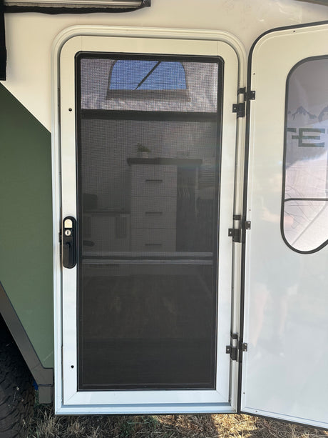 A white screen door with black mesh and handle on an RV rental, offering fresh air for your camping adventure.