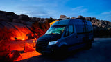 RV rental for a desert escape: A blue campervan parked at twilight in Joshua Tree, rocks glowing from a campfire.