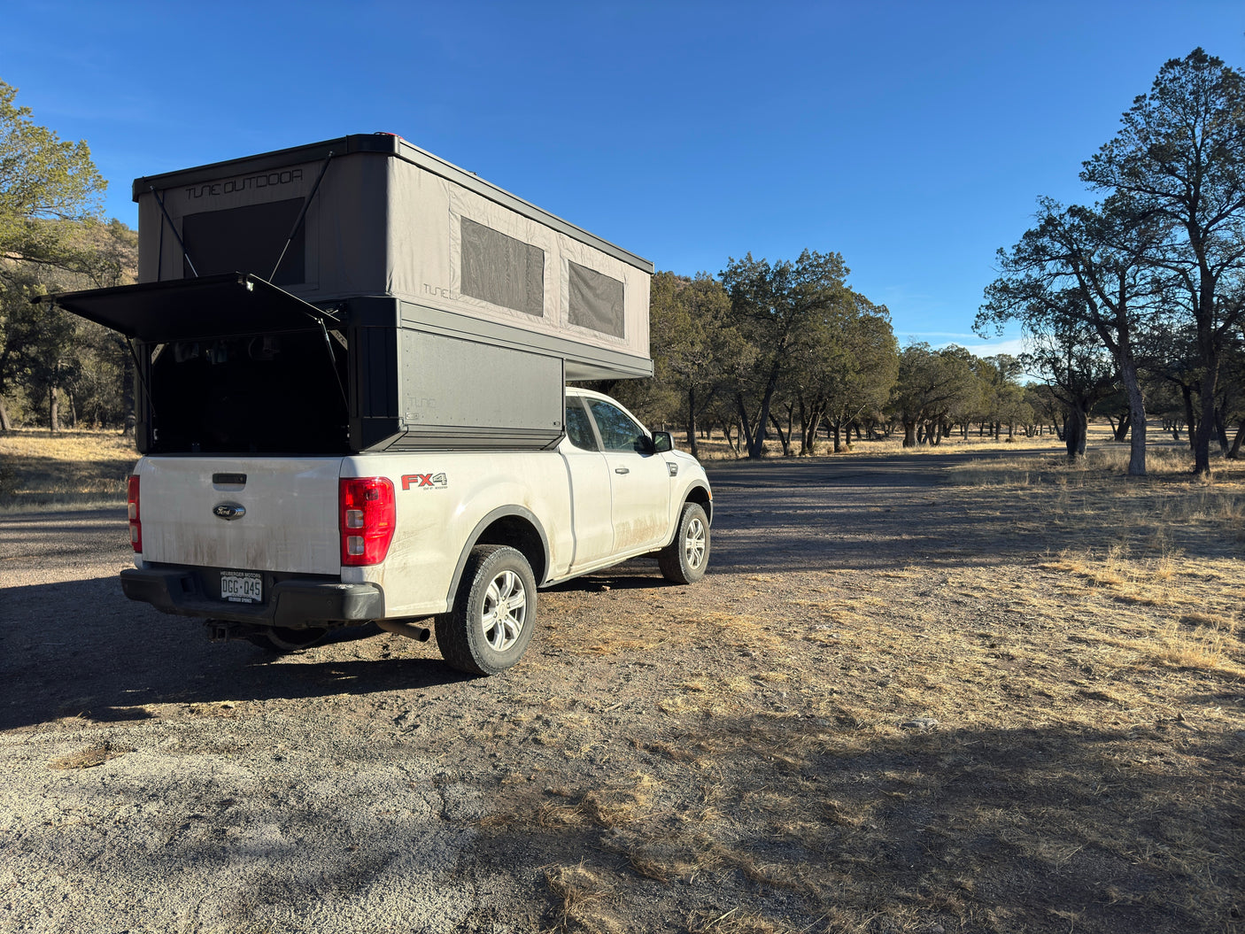 White Ford Ranger truck with an overland camper, resembling an RV rental, parked near Mammoth Hot Springs, Yellowstone.
