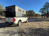 White Ford Ranger truck with an overland camper, resembling an RV rental, parked near Mammoth Hot Springs, Yellowstone.