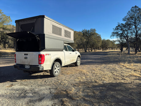 White Ford Ranger truck with an overland camper, resembling an RV rental, parked near Mammoth Hot Springs, Yellowstone.