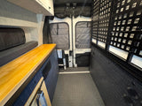 Explore this RV rental's camper van interior: wood counter, bench bed, and grid storage optimize adventure travel.