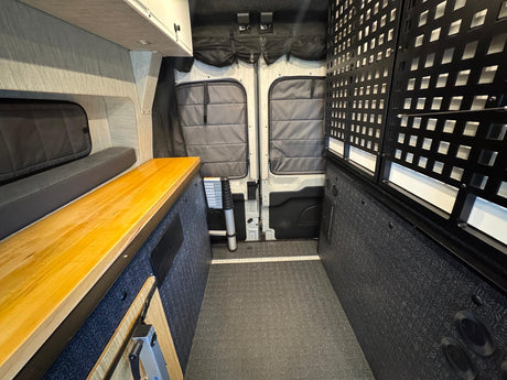 Explore this RV rental's camper van interior: wood counter, bench bed, and grid storage optimize adventure travel.