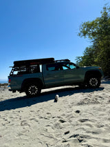 Adventure-ready grey Toyota Tacoma truck with rooftop tent parked on a sandy beach. Great for an rv rental outdoor escape!