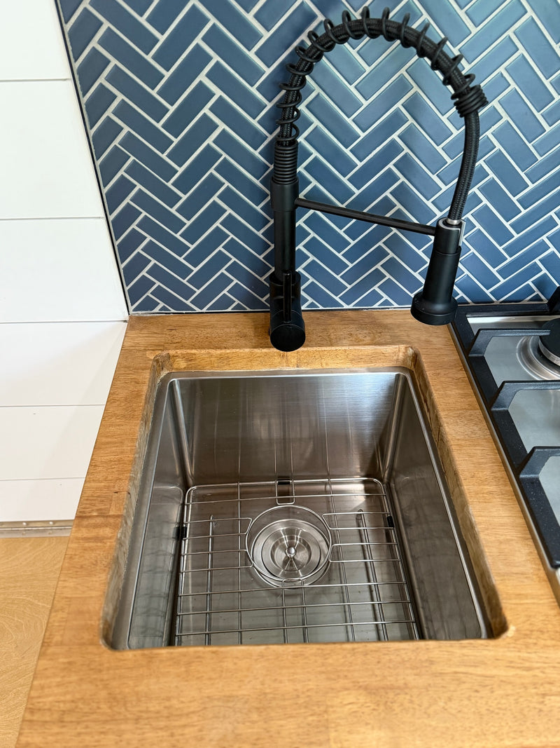 Modern RV rental kitchen featuring a stainless steel sink, wood counter, black faucet, and blue herringbone tile backsplash. — photo 18
