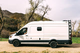White RV rental van on a dirt road, driver visible. Scenic mountains & trees. Perfect for adventure & van life.