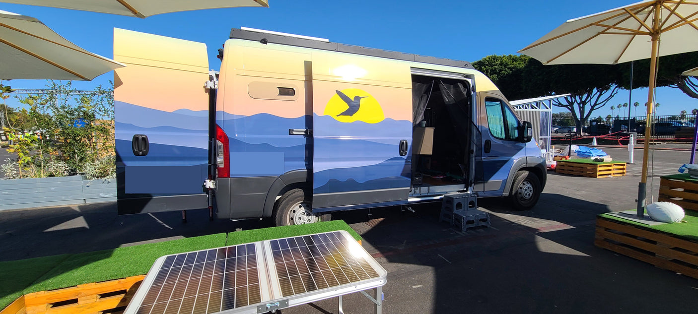 This colorful RV rental, adorned with mountain art & a hummingbird, displays an open interior and a portable solar panel.