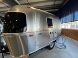A sleek Airstream Bambi travel trailer, ready for an rv rental, is parked indoors with a power cord connected.