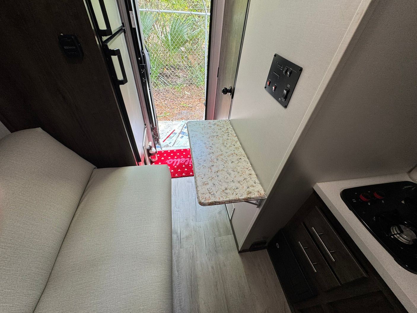 Inside an RV rental: light gray seating, wood-look floor, and a compact kitchen with a fold-down table near the open door.