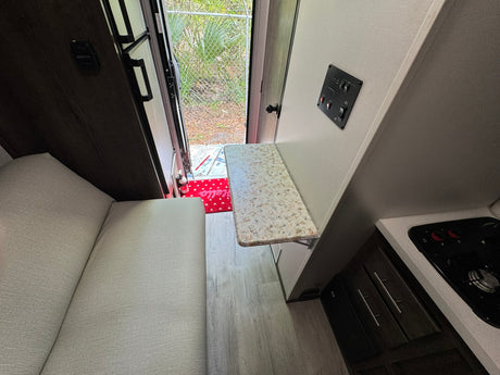 Inside an RV rental: light gray seating, wood-look floor, and a compact kitchen with a fold-down table near the open door.