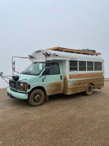 Cozy RV rental interior with light wood walls, mint green cabinetry, bunk bed with safety net, and tiled shower.