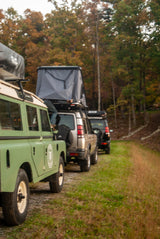 Green, silver, and black Land Rovers with rooftop tents, parked on a path. Great for an RV rental adventure!